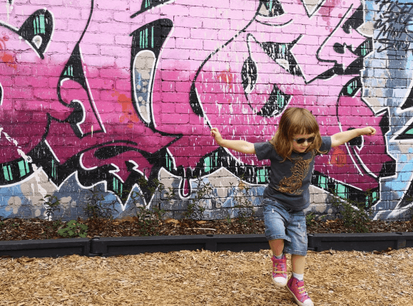 3 year old girl dancing in front of graffitied wall